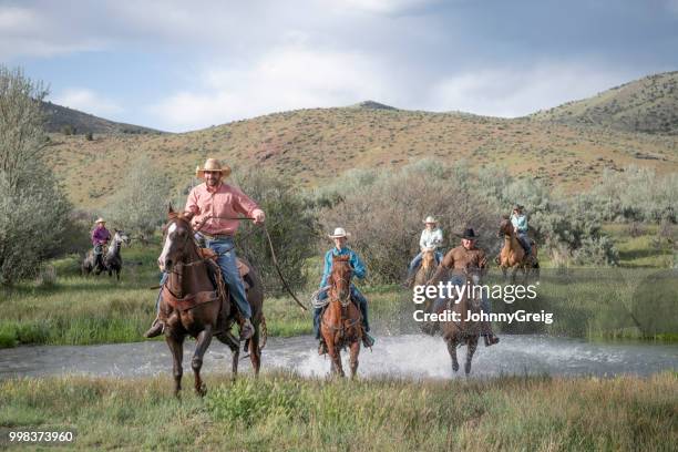 cowboys und cowgirls, die überquerung des flusses auf reiten spritzwasser durch wasser - johnny greig stock-fotos und bilder