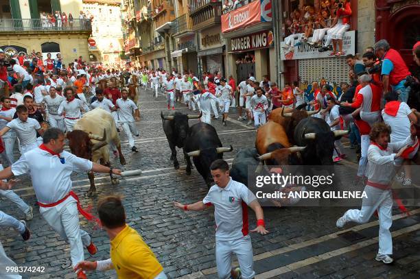 Miura fighting bulls fall over a runner on the last bullrun of the San Fermin festival in Pamplona, northern Spain on July 14, 2018. - Each day at...