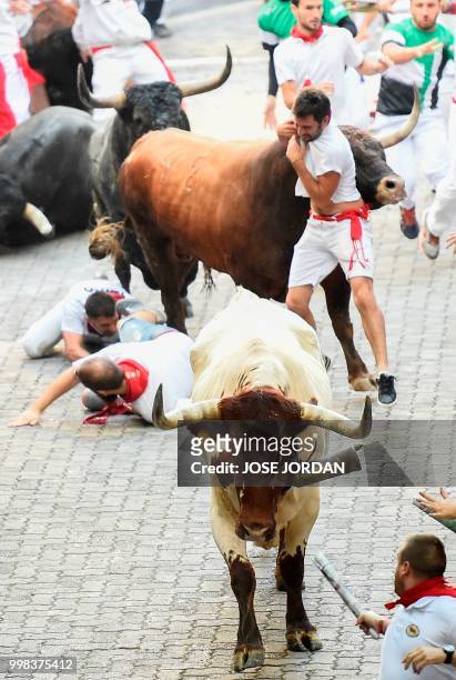 Participants fall next to Miura fighting bulls on the last bullrun of the San Fermin festival in Pamplona, northern Spain on July 14, 2018. - Each...