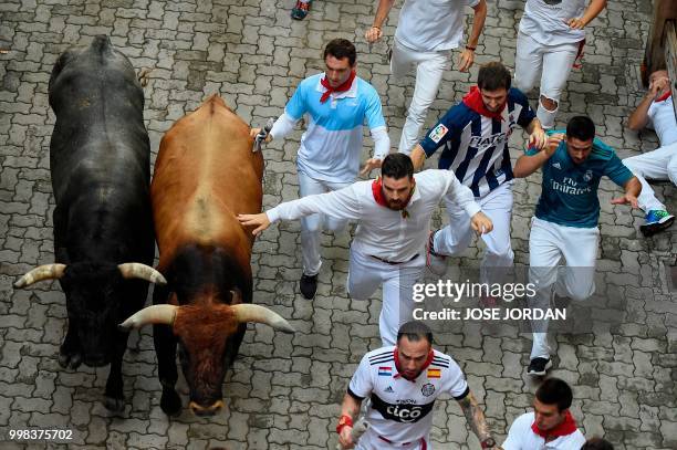 Participants run next to Miura fighting bulls on the last bullrun of the San Fermin festival in Pamplona, northern Spain on July 14, 2018. - Each day...