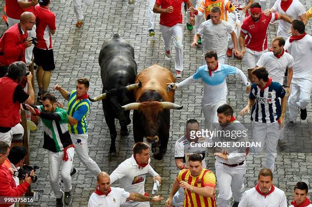 Participants run next to Miura fighting bulls on the last bullrun of the San Fermin festival in Pamplona, northern Spain on July 14, 2018. - Each day...