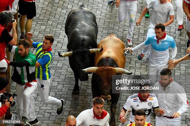 Participants run next to Miura fighting bulls on the last bullrun of the San Fermin festival in Pamplona, northern Spain on July 14, 2018. - Each day...