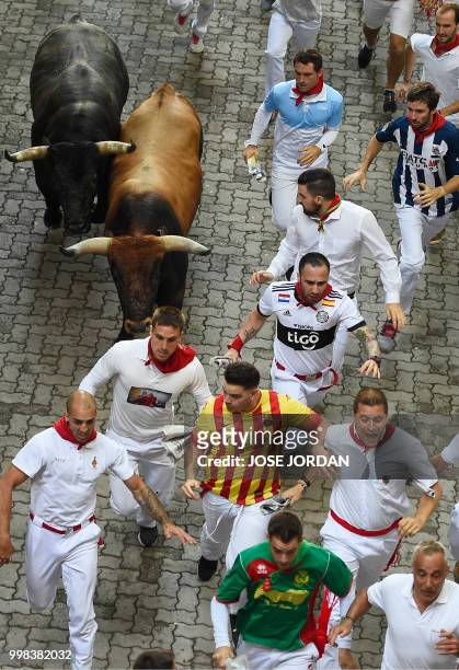 Participants run next to Miura fighting bulls on the last bullrun of the San Fermin festival in Pamplona, northern Spain on July 14, 2018. - Each day...