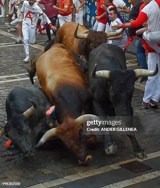 Miura fighting bulls fall over a runner during the last bullrun of the San Fermin festival in Pamplona, northern Spain on July 14, 2018. - Each day...