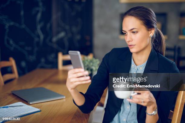 junge geschäftsfrau mit mobiltelefon mit kaffeepause - emir memedovski stock-fotos und bilder