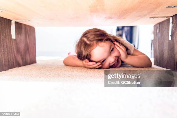 playful baby girl playing hiding under a table - mischief stock pictures, royalty-free photos & images