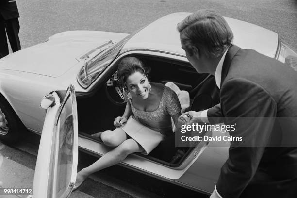 English actress, author and columnist Joan Collins stepping out of a car with the help of American actor George Peppard during filming of 'The...