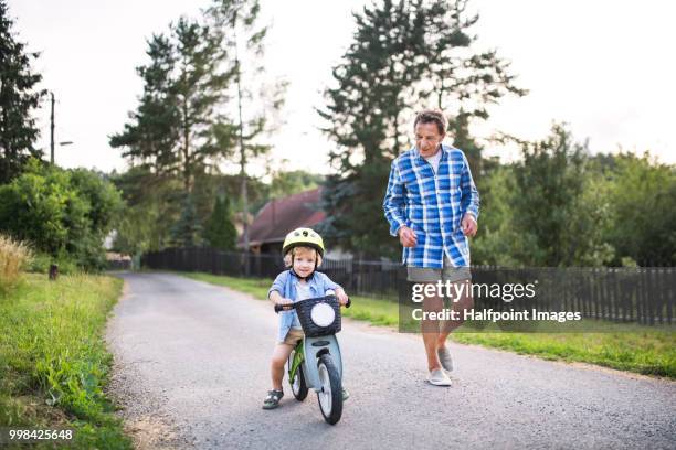 a small toddler boy with his grandfather riding a balance bike outdoors. - halfpoint stockfoto's en -beelden