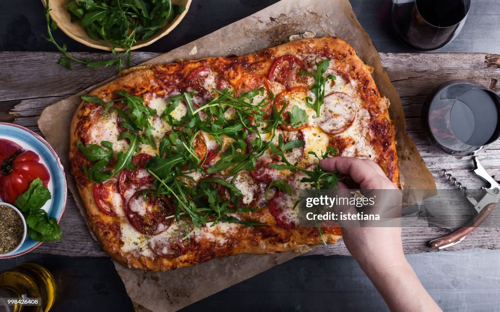 Preparing gourmet pizza, close-up of hand topping pizza with arugula