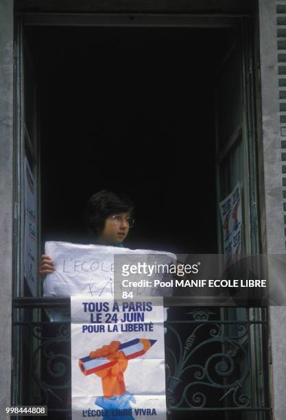 Jeune à la fenêtre tenant une pancarte lors de la manifestation pour l'école libre à Paris le 24 juin 1984, France.