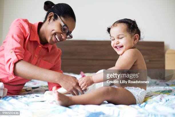 Mother and child laughing together while child is getting dressed