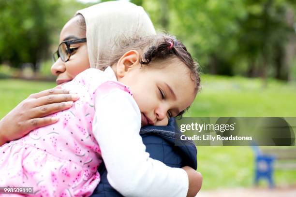 mother carrying sleeping young child in park - lilly roadstones stock pictures, royalty-free photos & images