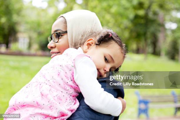 mother carrying young child in public park - lilly roadstones stock pictures, royalty-free photos & images