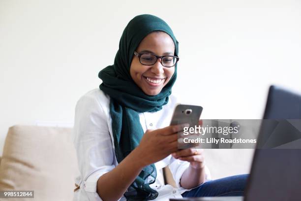 young muslim woman using mobile phone and laptop - lilly roadstones stock pictures, royalty-free photos & images