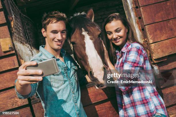 due giovani che si fanno selfie mentre accarezzano il cavallo marrone - emir memedovski foto e immagini stock