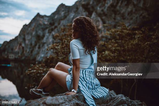 porträt von sinnlich weiblichen sitzt auf einer klippe in der nähe von bergsee während des sonnenuntergangs - aleksandar georgiev stock-fotos und bilder