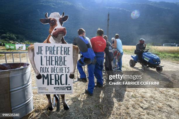 People stand next to a banner showing a cow figure and reading "I prefer grass to waste", as a participant rides a lawn-mower during the 5th edition...