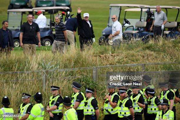 Police secure the area as U.S. President Donald Trump, wearing a hat with Trump and USA displayed on it, waves while playing golf at Trump Turnberry...