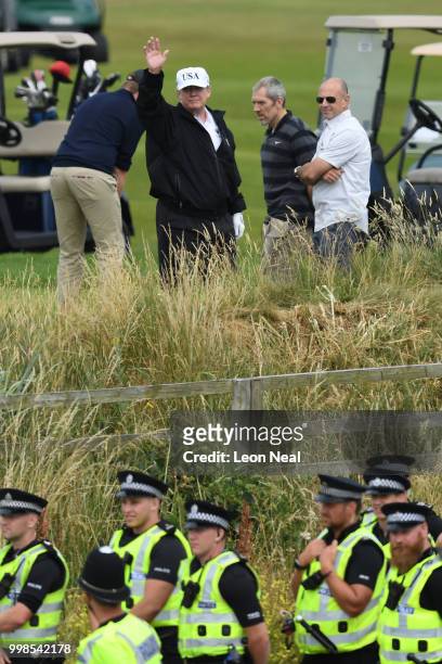 Police secure the area as U.S. President Donald Trump, wearing a hat with Trump and USA displayed on it, waves while playing golf at Trump Turnberry...