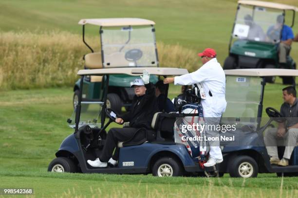 President Donald Trump, wearing a hat with Trump and USA displayed on it, waves while ride a cart playing golf at Trump Turnberry Luxury Collection...