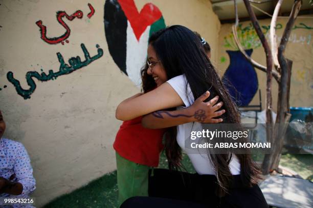 Palestinian girl from the Bedouin village of Khan al-Ahmar in the occupied West Bank embraces as a woman after having had her face painted, during...