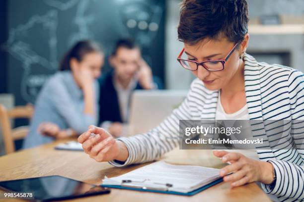 businesswoman in the office trying to read business report - emir memedovski stock pictures, royalty-free photos & images