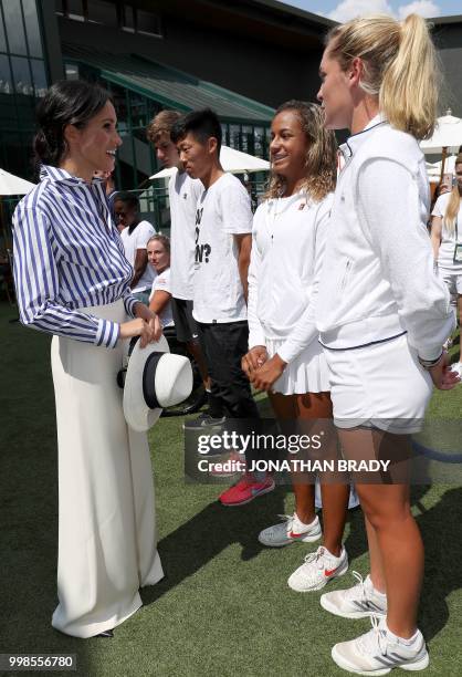 Britain's Meghan, Duchess of Sussex talk to ball boys and girls, and junior players as they arrive to watch the women's final match on the twelfth...