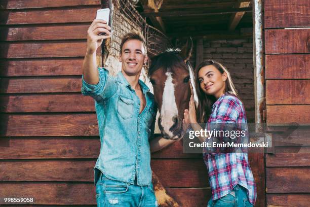 two young people taking selfie while stroking brown horse - emir memedovski stock pictures, royalty-free photos & images