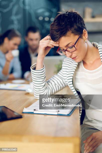 overworked businesswoman in the office trying to read business report - emir memedovski stock pictures, royalty-free photos & images