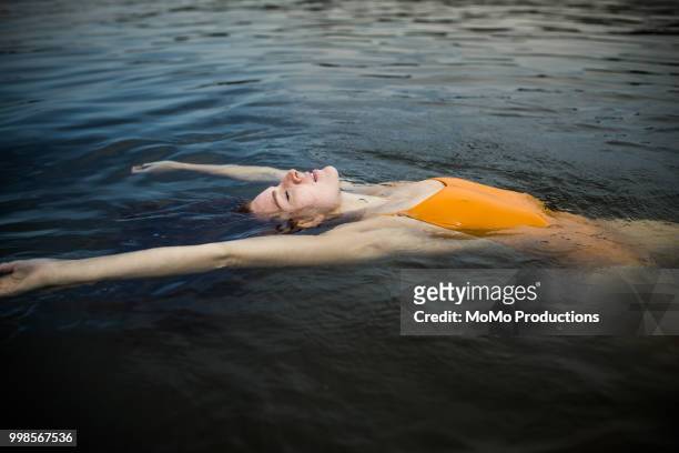 young woman floating in the water at lake - swimming stock-fotos und bilder