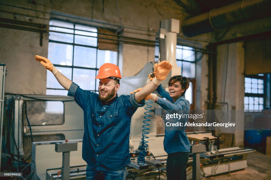 Female Carpenter Blowing Sawdust Off Male Colleague After Work