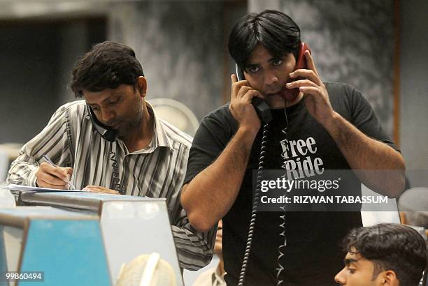 Pakistani stockbrokers talk on their phones during a trading session at the Karachi Stock Exchange on May 18, 2010. The benchmark KSE-100 index was...