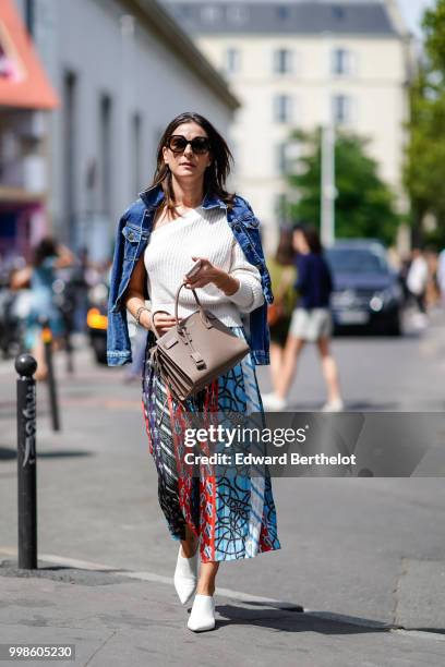 Guest wears a blue denim jacket, a white pullover, a brown Saint Laurent YSL bag, a multicolor printed pattern pleated skirt, white sneakers shoes,...