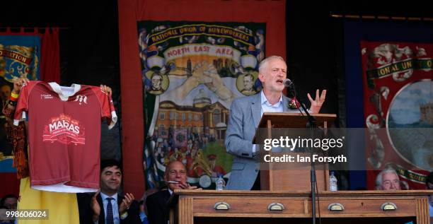 Labour Leader Jeremy Corbyn delivers his speech as Laura Alvarez holds up a Friends of Durham Miners Gala, the 'Marra's' shirt during the 134th...