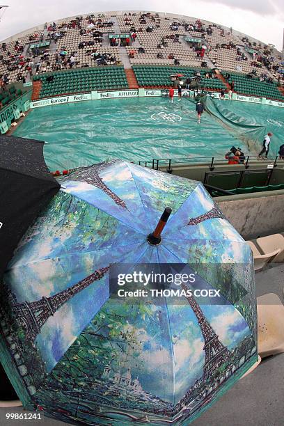 People wait in Roland Garros' Suzanne Lenglen court as maintenance workers cover the court on the second day of the French Tennis Open, 28 May 2007...