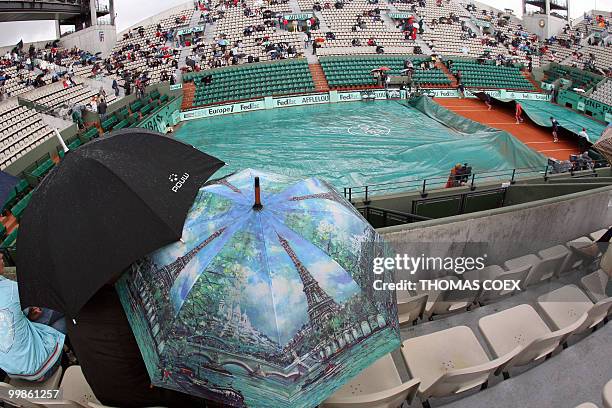 People wait in Roland Garros' Suzanne Lenglen court as maintenance workers cover the court on the second day of the French Tennis Open, 28 May 2007...