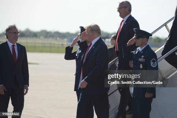 President Donald J Trump returns salute to military members as he is greeted by North Dakota Governor Doug Burgum, left, upon his arrival at the...