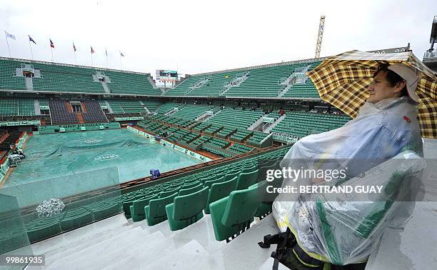 Spectator wrapped in plastic and holding an umbrella sits on centre court during the French Open tennis first round matches on May 26, 2009 at Roland...