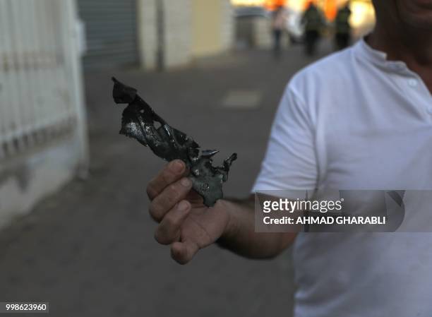 Resident of the southern Israeli city of Sderot holds a piece of shrapnel from a rocket fired from the Gaza Strip on July 14, 2018. - Rockets were...