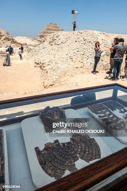 Picture taken on July 14, 2018 shows a broken gilded mummy mask on display in front of the step pyramid of Saqqara, south of the Egyptian capital...