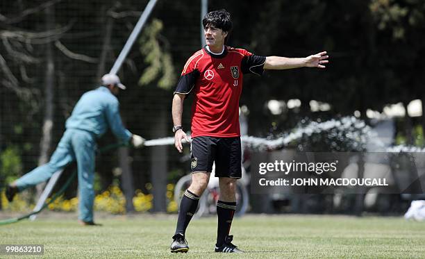 Germany's head coach Joachim Loew speaks to his players as a worker sprays the pitch during a training session at the Verdura Golf and Spa resort,...