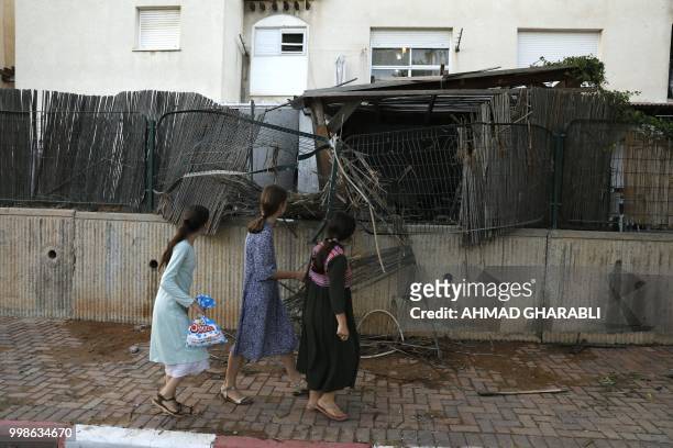 Young residents of the southern Israeli city of Sderot walk in front of a fence damaged by a rocket fired from the Gaza Strip on July 14, 2018. -...