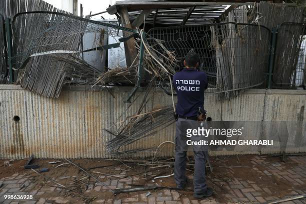 An Israeli policeman inspects a fence damaged by a rocket, fired from the Gaza Strip on July 14 in the southern Israeli city of Sderot. - Israel...