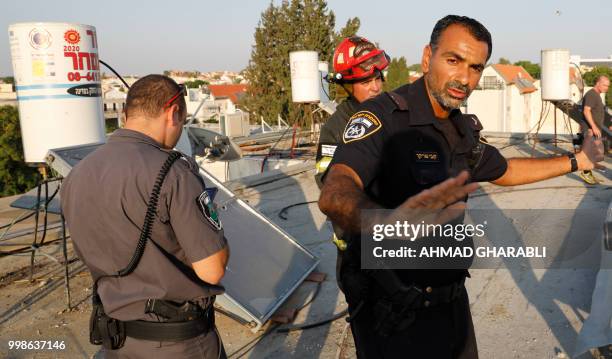 Member of the Israeli security forces gestures as another inspects with a fire fighter the damage on the rooftop of a building in the southern...