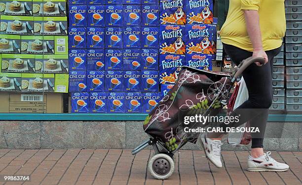 Woman pulls her shopping basket as she walks past a store displaying food and drinks goods in it's window, in Hounslow, west London on May 18, 2010....