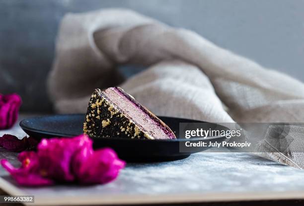 piece of dark chocolate mousse cake with rose petal blackberry jam and nuts on a black plate and... - aubergine blanche photos et images de collection