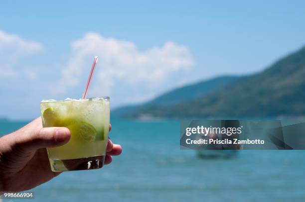 hand holding glass of caipirinha on the beach. paraty, rj, brazil - caipirinha stock-fotos und bilder