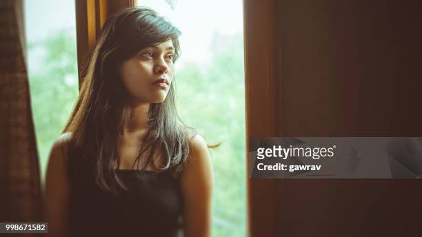 mooie serene jonge vrouw denkt in de buurt van venster. - 16x9 beeldverhouding stockfoto's en -beelden
