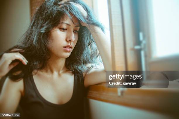 sad young woman thinks near window. - gawrav stock pictures, royalty-free photos & images