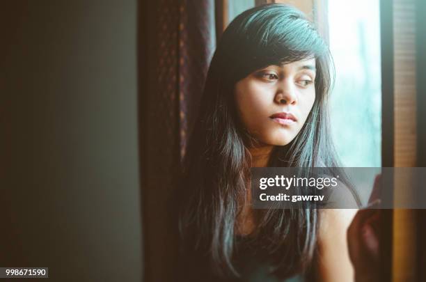 beautiful serene young woman thinks near window. - gawrav stock pictures, royalty-free photos & images